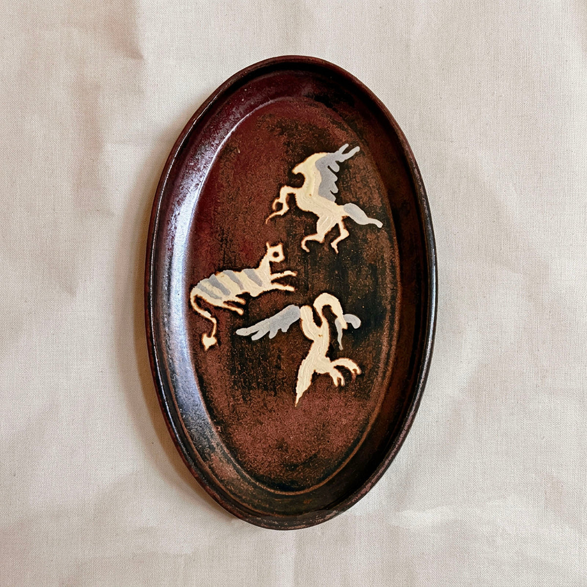 Oval oxblood and black glazed platter with three cream and grey Pompeii-inspired winged creatures