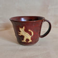 Oxblood-red mug with a cream slip-relief rabbit and cat motif