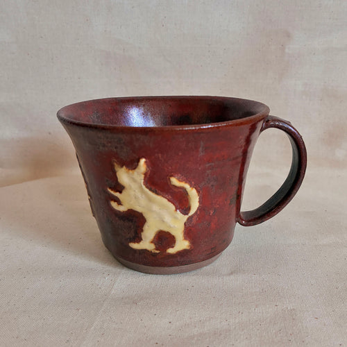 Oxblood-red mug with a cream slip-relief rabbit and cat motif